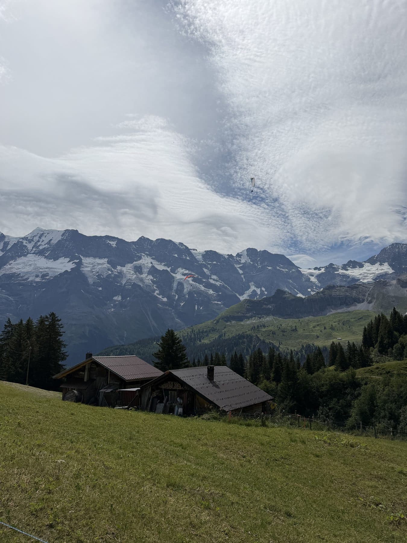 Alphütten und Berge mit Gleitschirmfliegern am Himmel